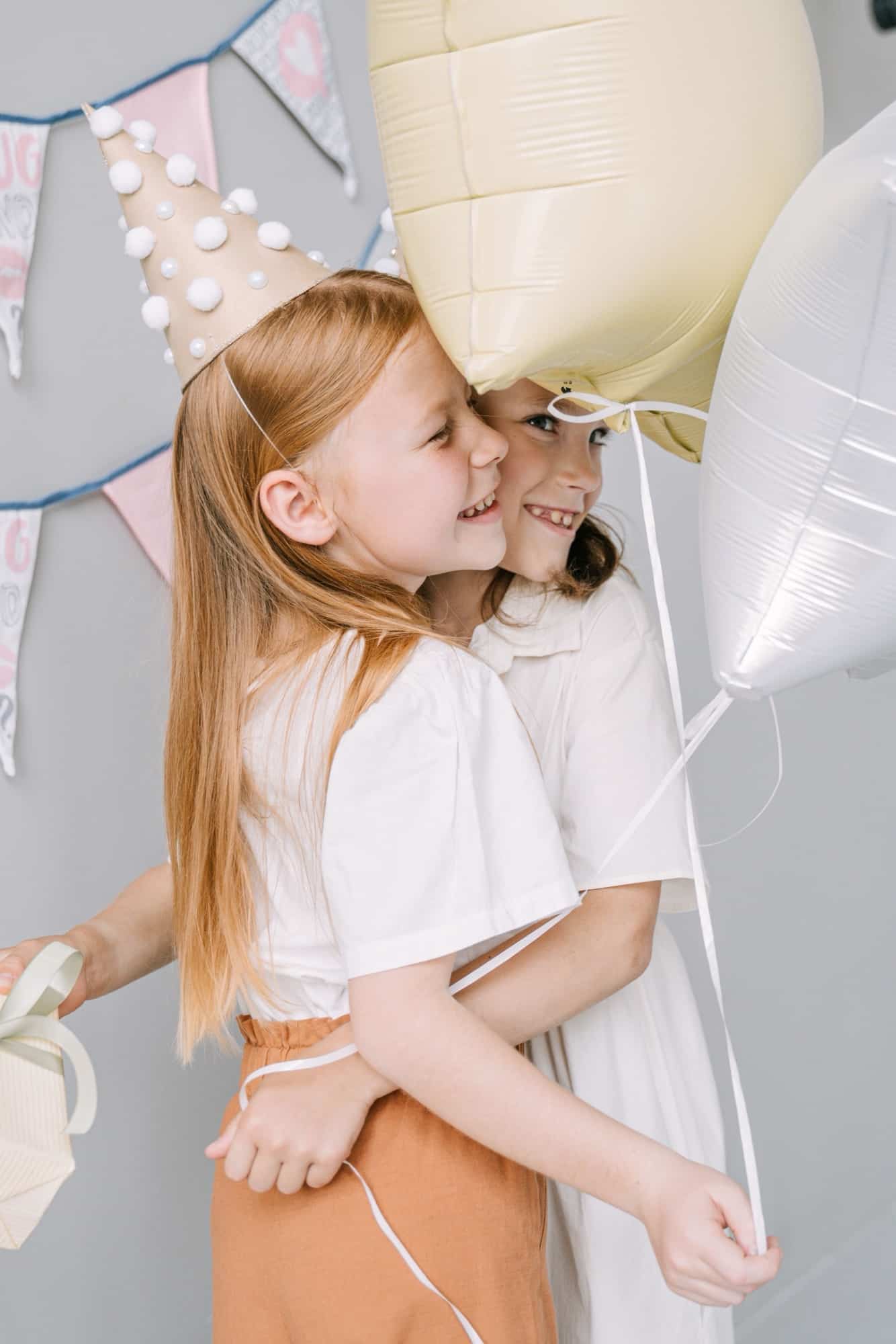 Deux fillettes souriantes à un anniversaire, chapeau de fête et ballons pastel