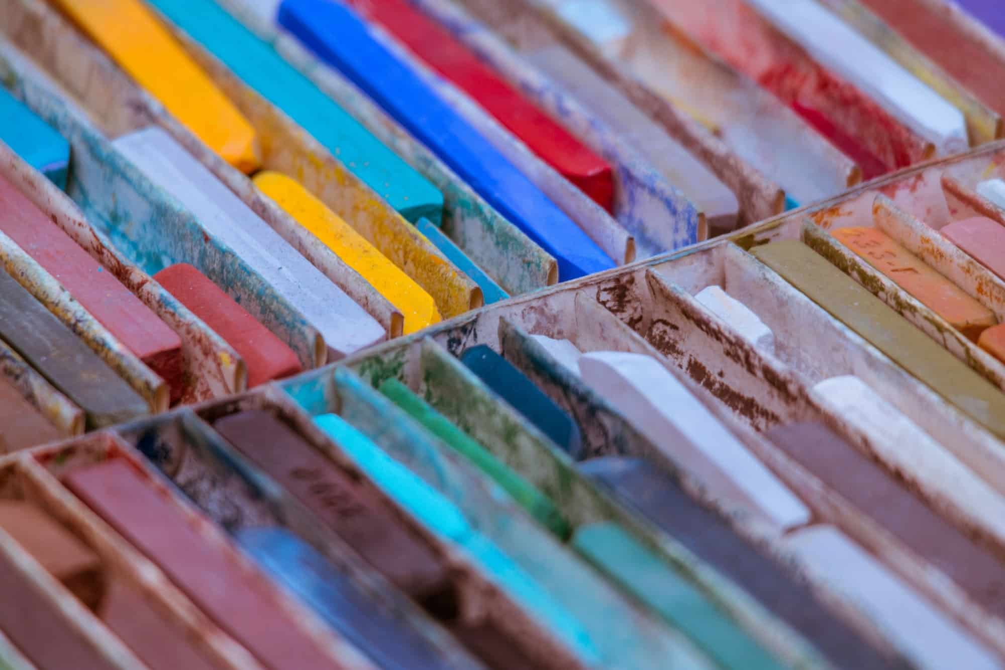 Gros plan sur des pastels d'artiste alignés dans leur coffret, aux couleurs vives