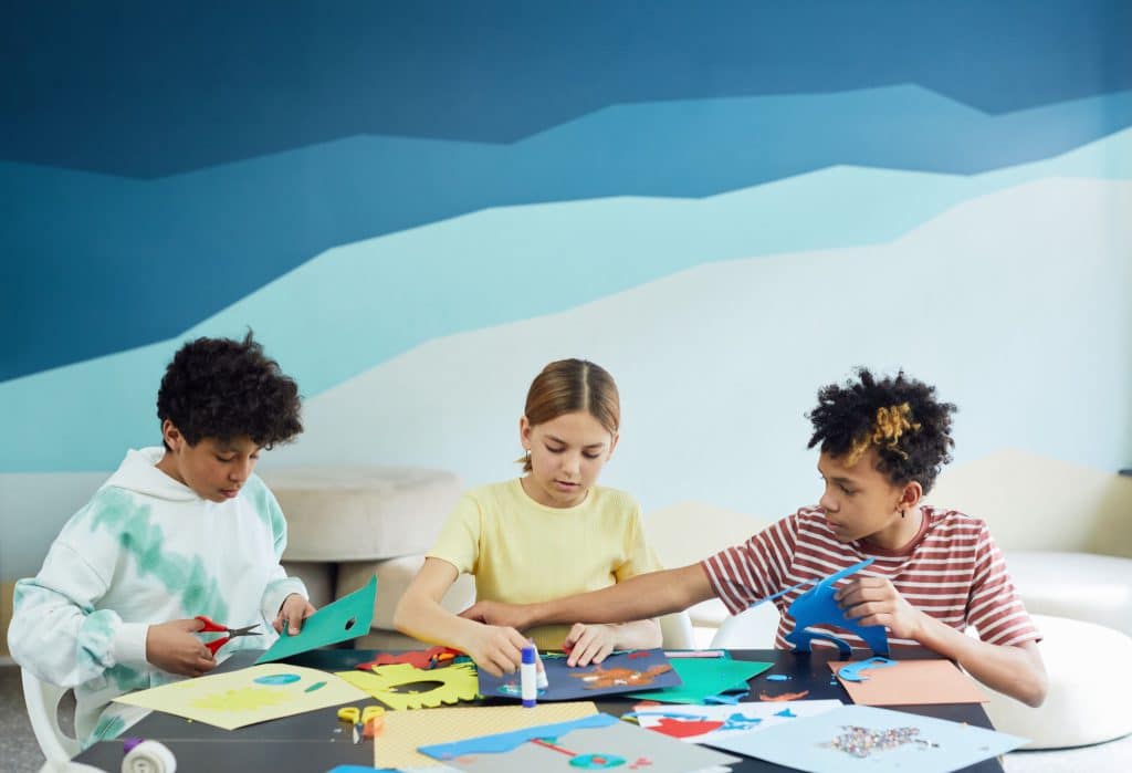 Trois enfants découpent du papier coloré autour d'une table d'atelier